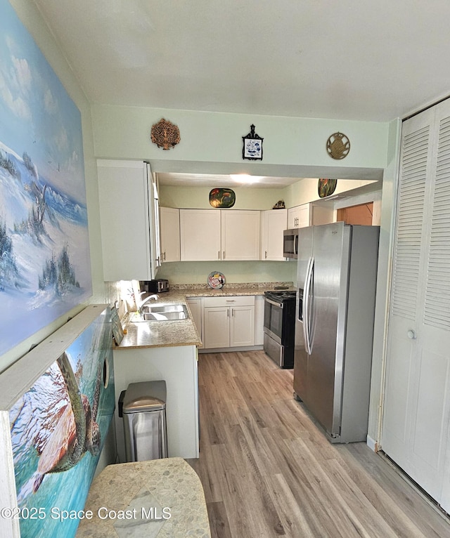 kitchen featuring light wood-style flooring, stainless steel appliances, a sink, white cabinetry, and light countertops