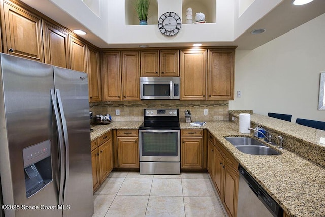 kitchen featuring brown cabinets, light stone counters, stainless steel appliances, and a sink