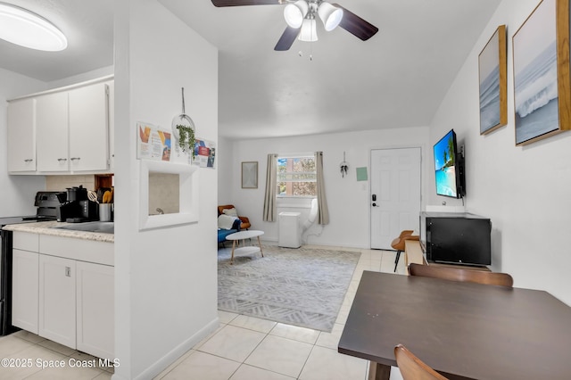 interior space with light tile patterned floors, a ceiling fan, white cabinets, black electric range, and light countertops
