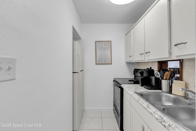 kitchen featuring black range with electric stovetop, a sink, freestanding refrigerator, and white cabinets
