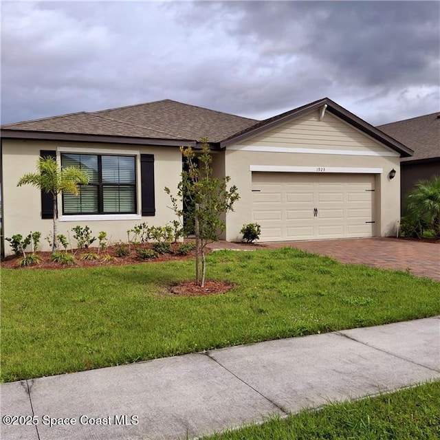 ranch-style home featuring roof with shingles, an attached garage, decorative driveway, a front yard, and stucco siding