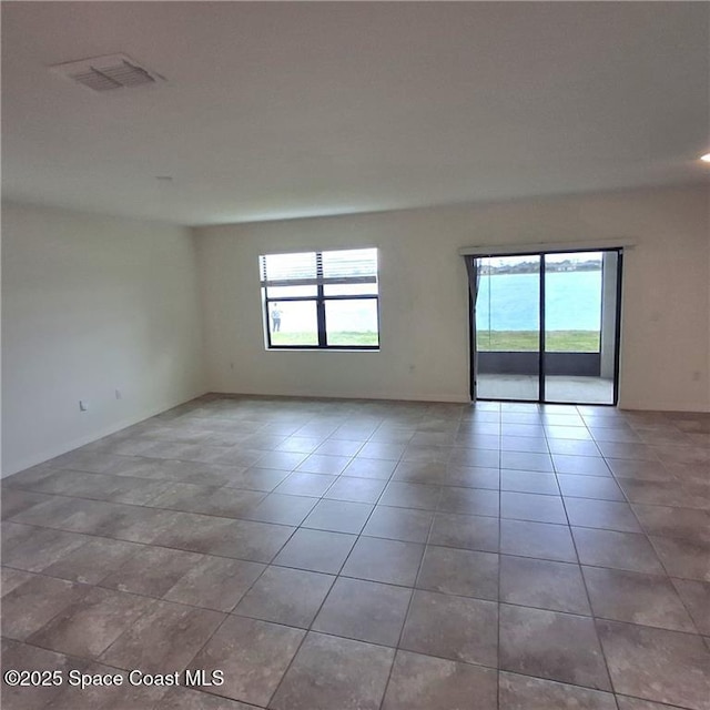 tiled spare room featuring a healthy amount of sunlight and visible vents