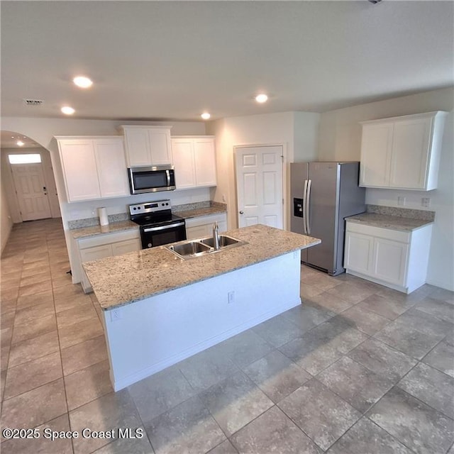 kitchen with arched walkways, a sink, white cabinets, appliances with stainless steel finishes, and an island with sink