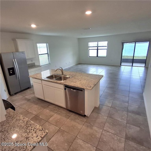 kitchen featuring light stone counters, a kitchen island with sink, stainless steel appliances, a sink, and white cabinetry