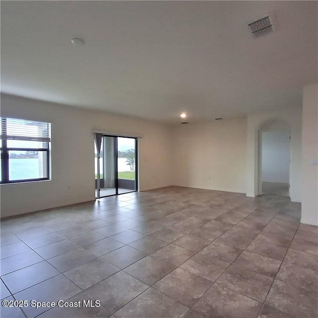 unfurnished room featuring light tile patterned floors, visible vents, and arched walkways