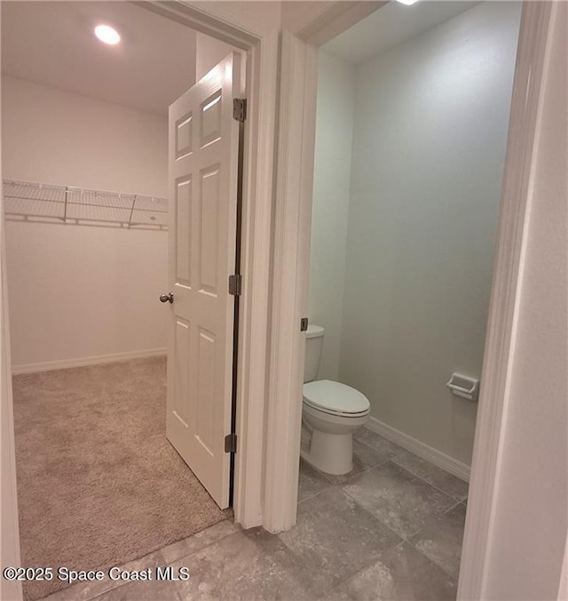 bathroom with a walk in closet, baseboards, and toilet