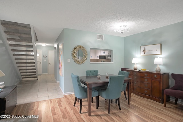 dining area featuring a textured ceiling, visible vents, baseboards, stairs, and light wood-type flooring