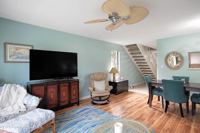 living area featuring a textured ceiling, ceiling fan, stairway, and wood finished floors