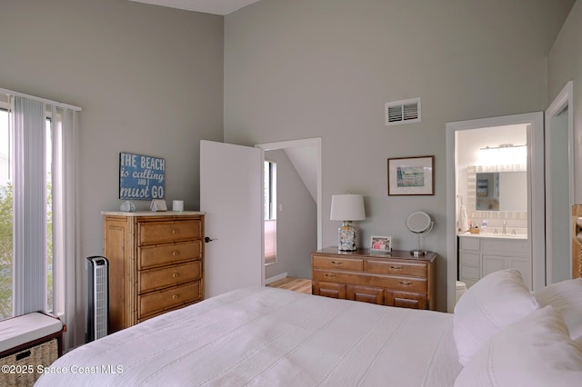 bedroom with connected bathroom, a high ceiling, visible vents, and a sink