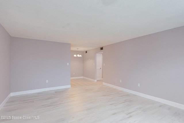 empty room featuring a chandelier, light wood-type flooring, and baseboards