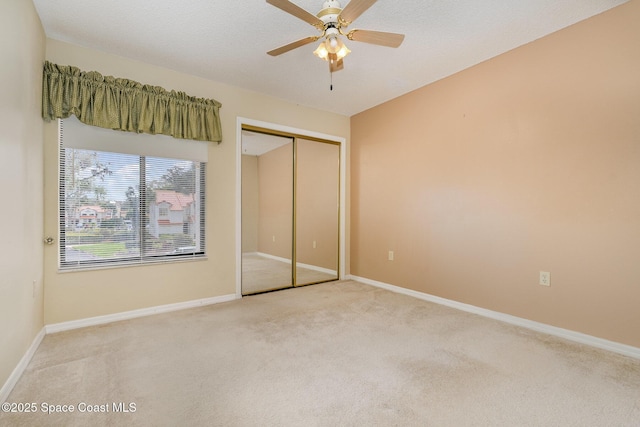 unfurnished bedroom featuring ceiling fan, a textured ceiling, light colored carpet, baseboards, and a closet