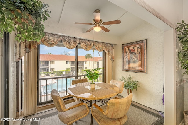 dining room featuring a ceiling fan, vaulted ceiling, and a textured wall