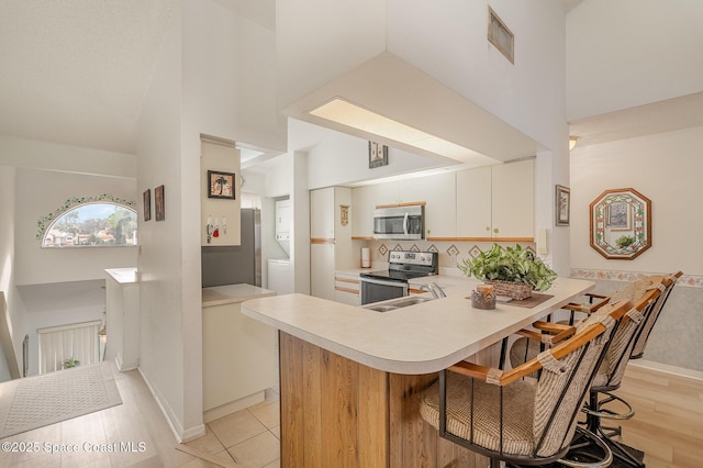 kitchen with a peninsula, a towering ceiling, stainless steel appliances, and light countertops