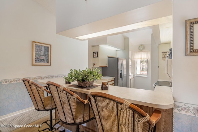 kitchen featuring light countertops, wood finished floors, stainless steel fridge, a peninsula, and baseboards