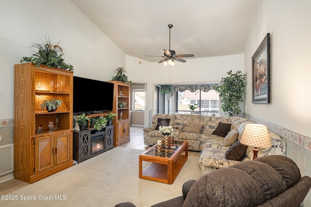 living room with a ceiling fan, a glass covered fireplace, light carpet, and high vaulted ceiling