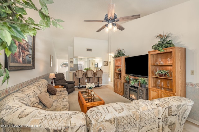 living room with a ceiling fan, a glass covered fireplace, visible vents, and a high ceiling