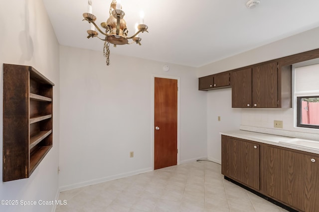 kitchen featuring a sink, light countertops, dark brown cabinets, a chandelier, and backsplash