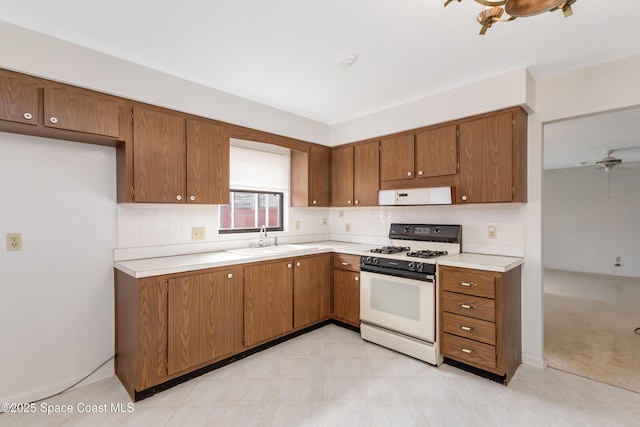 kitchen with brown cabinets, white range with gas cooktop, light countertops, and a sink