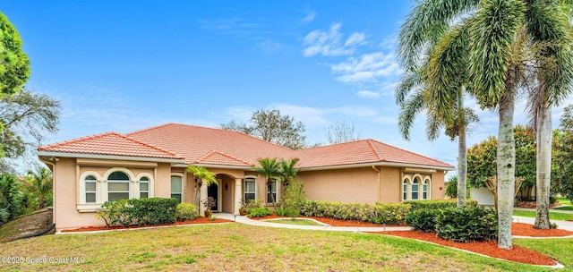 mediterranean / spanish home featuring a front yard, a tiled roof, and stucco siding