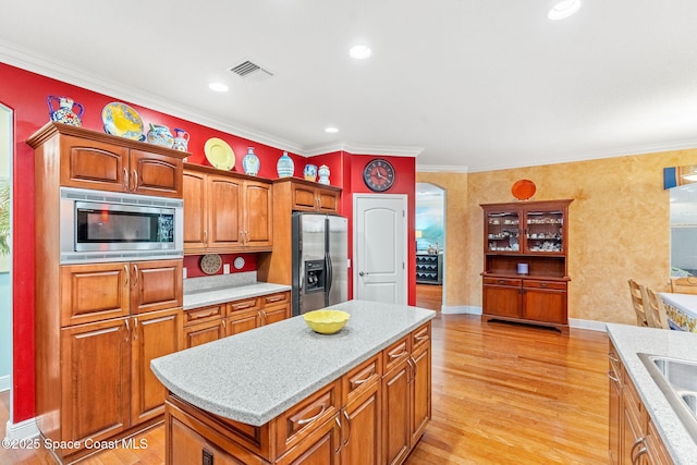 kitchen featuring visible vents, light wood-style flooring, appliances with stainless steel finishes, brown cabinets, and a center island