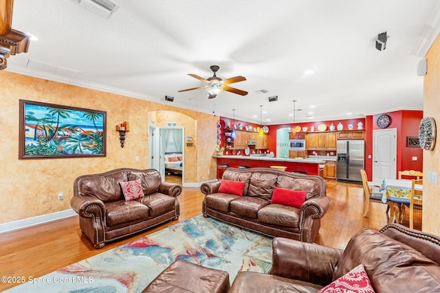 living area with arched walkways, light wood-style flooring, visible vents, baseboards, and ornamental molding