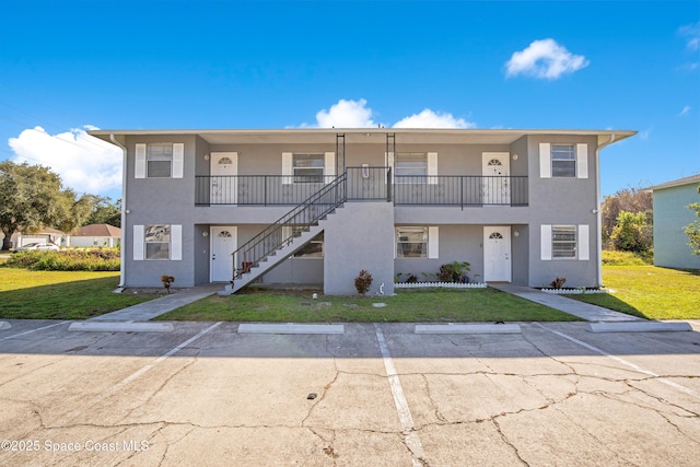 view of front of house with uncovered parking, a front lawn, stairway, and stucco siding