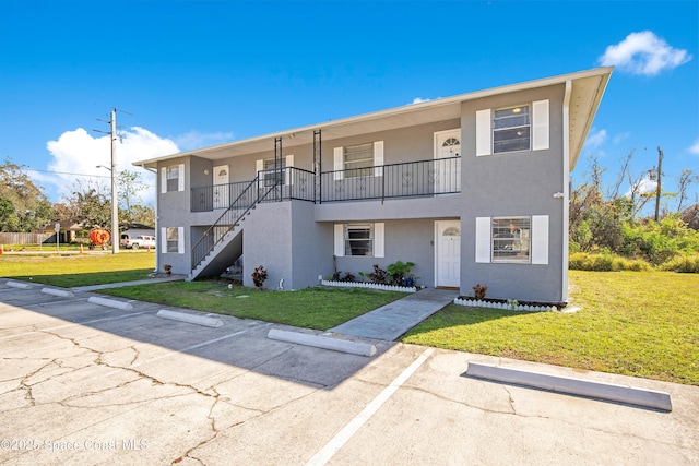 view of front of home with uncovered parking, stucco siding, a front lawn, and stairs