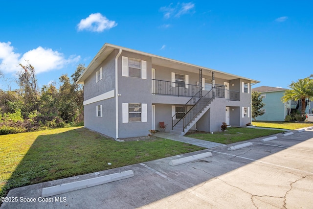 view of front facade featuring uncovered parking, a front yard, stairway, and stucco siding