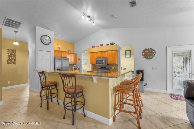 kitchen featuring stone counters, a breakfast bar, light tile patterned floors, stainless steel appliances, and visible vents