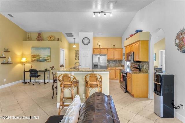 kitchen featuring light tile patterned floors, light stone counters, stainless steel appliances, visible vents, and a center island