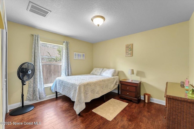 bedroom with baseboards, a textured ceiling, visible vents, and dark wood-type flooring