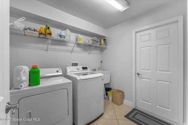 washroom featuring light tile patterned floors, a textured ceiling, laundry area, a sink, and washer and clothes dryer