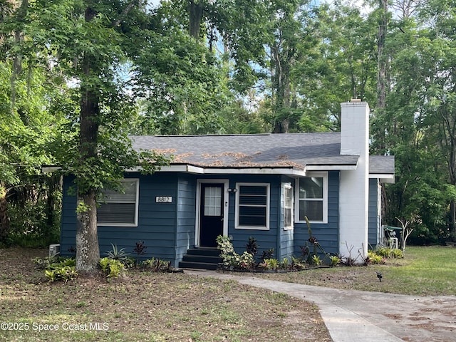 ranch-style home featuring a chimney and roof with shingles