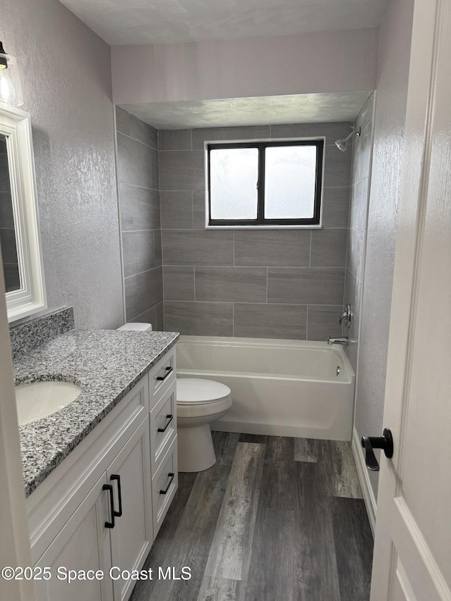 bathroom featuring a textured wall, bathtub / shower combination, toilet, wood finished floors, and vanity