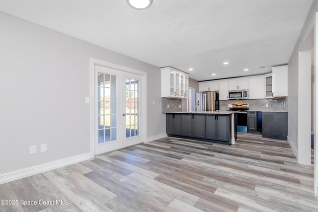 kitchen with dark countertops, decorative backsplash, appliances with stainless steel finishes, glass insert cabinets, and white cabinets