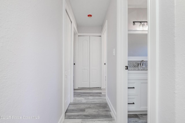 hallway with a sink, light wood-style flooring, and baseboards