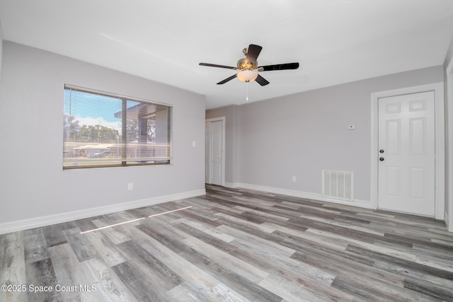 empty room with light wood finished floors, a ceiling fan, visible vents, and baseboards