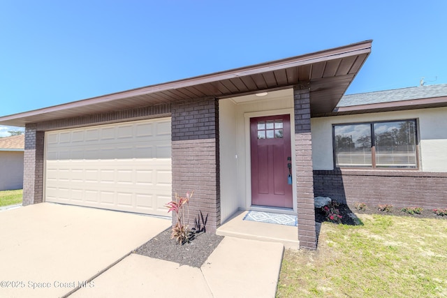 view of exterior entry with an attached garage, a yard, concrete driveway, and brick siding