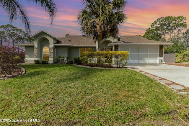 single story home with stucco siding, a garage, stone siding, driveway, and a front lawn