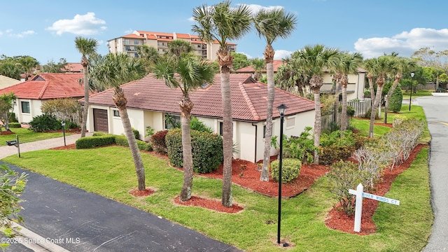 view of front facade with driveway, stucco siding, a front lawn, a garage, and a tiled roof