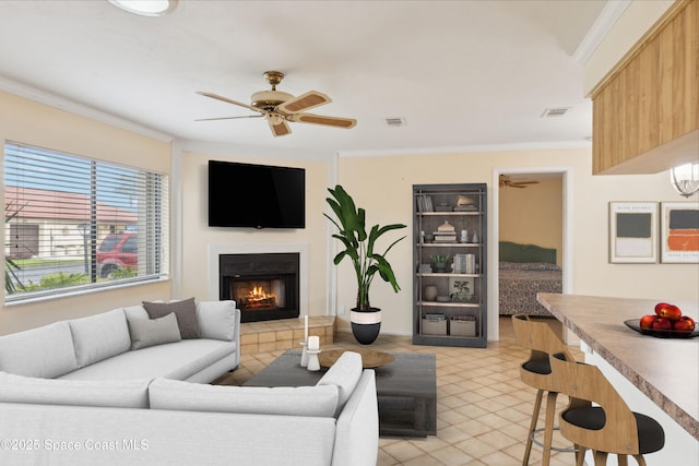 living area featuring a tiled fireplace, visible vents, crown molding, and a ceiling fan