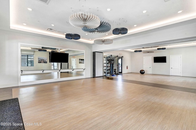 exercise room with wood finished floors, a raised ceiling, visible vents, and recessed lighting
