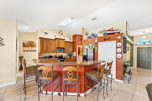 kitchen featuring light tile patterned floors, brown cabinetry, lofted ceiling, appliances with stainless steel finishes, and a breakfast bar area