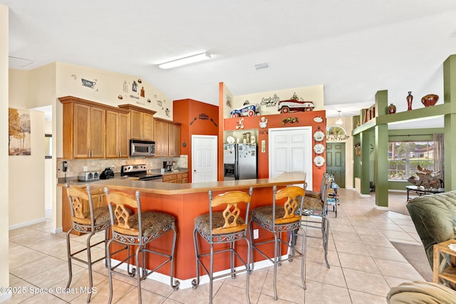 kitchen with light tile patterned floors, brown cabinets, a kitchen breakfast bar, vaulted ceiling, and stainless steel appliances