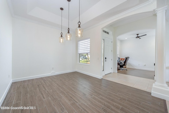 empty room with arched walkways, a tray ceiling, decorative columns, ceiling fan, and wood finished floors