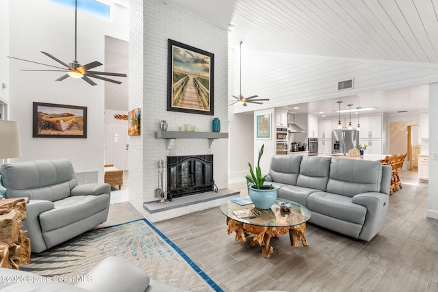 living area with high vaulted ceiling, a fireplace, light wood finished floors, and ceiling fan