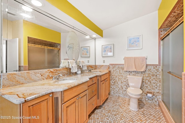 full bath featuring double vanity, tile walls, a sink, and toilet