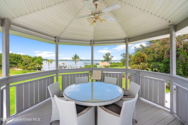 wooden terrace featuring a water view, a gazebo, outdoor dining area, and a ceiling fan