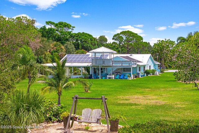 rear view of property featuring solar panels and a lawn