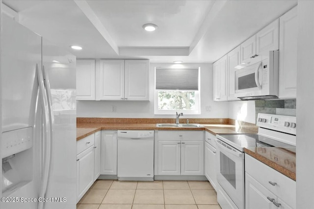 kitchen featuring a raised ceiling, white cabinetry, a sink, light tile patterned flooring, and white appliances